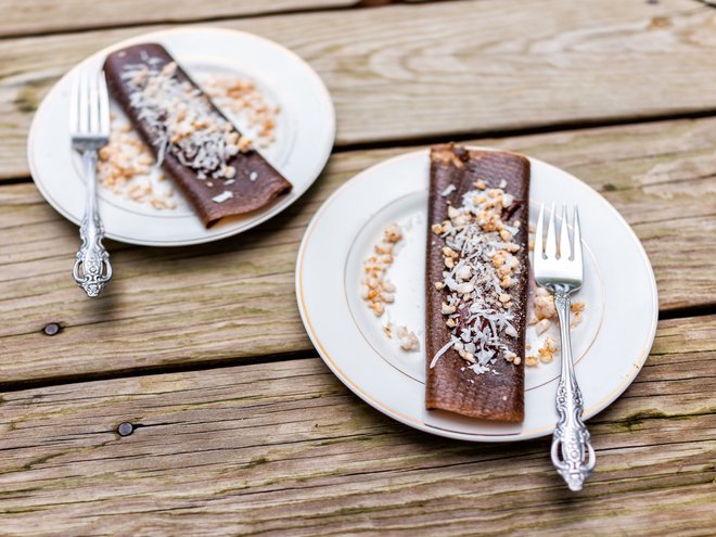 Closeup of two chocolate crepe dessert wraps with coconut flakes made in dehydrator with bananas on plates and forks