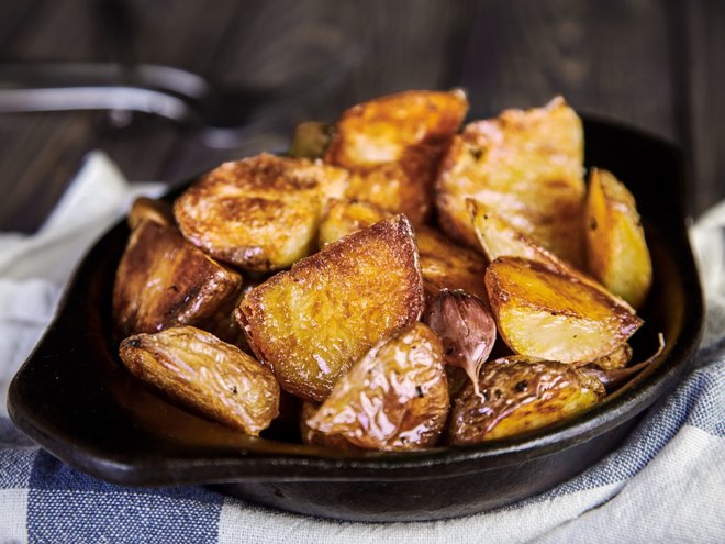Delicious hot baked potato wedges with garlic in black rustic plate on kitchen towel. Appetizing crisp. Traditional garnish or side dish for Christmas dinner. Country-style roasted potatoes (Delicious hot baked potato wedges with garlic in black rusti
